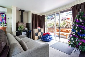 A living room with a sofa, a bean bag, a fireplace, a Christmas tree, and a sliding glass door leading to an outdoor patio. - Lakeview Family Home | Spa Pool | Sleeps 14 | 5 Min Town (Queenstown)
