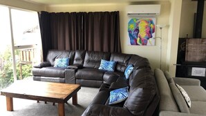 Ein Wohnzimmer mit einem braunen Ledersofa, einem Couchtisch aus Holz und einem grauen Sofa. An der Wand hängt ein farbenfrohes Gemälde und es gibt eine schwarze Unterhaltungsanlage.