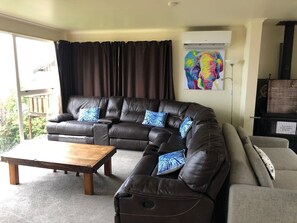 Ein Wohnzimmer mit einem braunen Ledersofa, einem Couchtisch aus Holz und einem grauen Sofa. An der Wand hängt ein farbenfrohes Gemälde und es gibt eine schwarze Unterhaltungsanlage.
