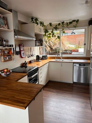 A modern kitchen with a wooden countertop, stainless steel appliances, and a window with a view of the outdoors. - Lakeview Family Home | Spa Pool | Sleeps 14 | 5 Min Town (Queenstown)