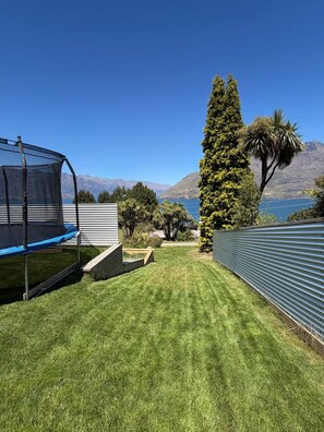Un jardin avec un trampoline, un grand arbre et une vue sur les montagnes et un lac.