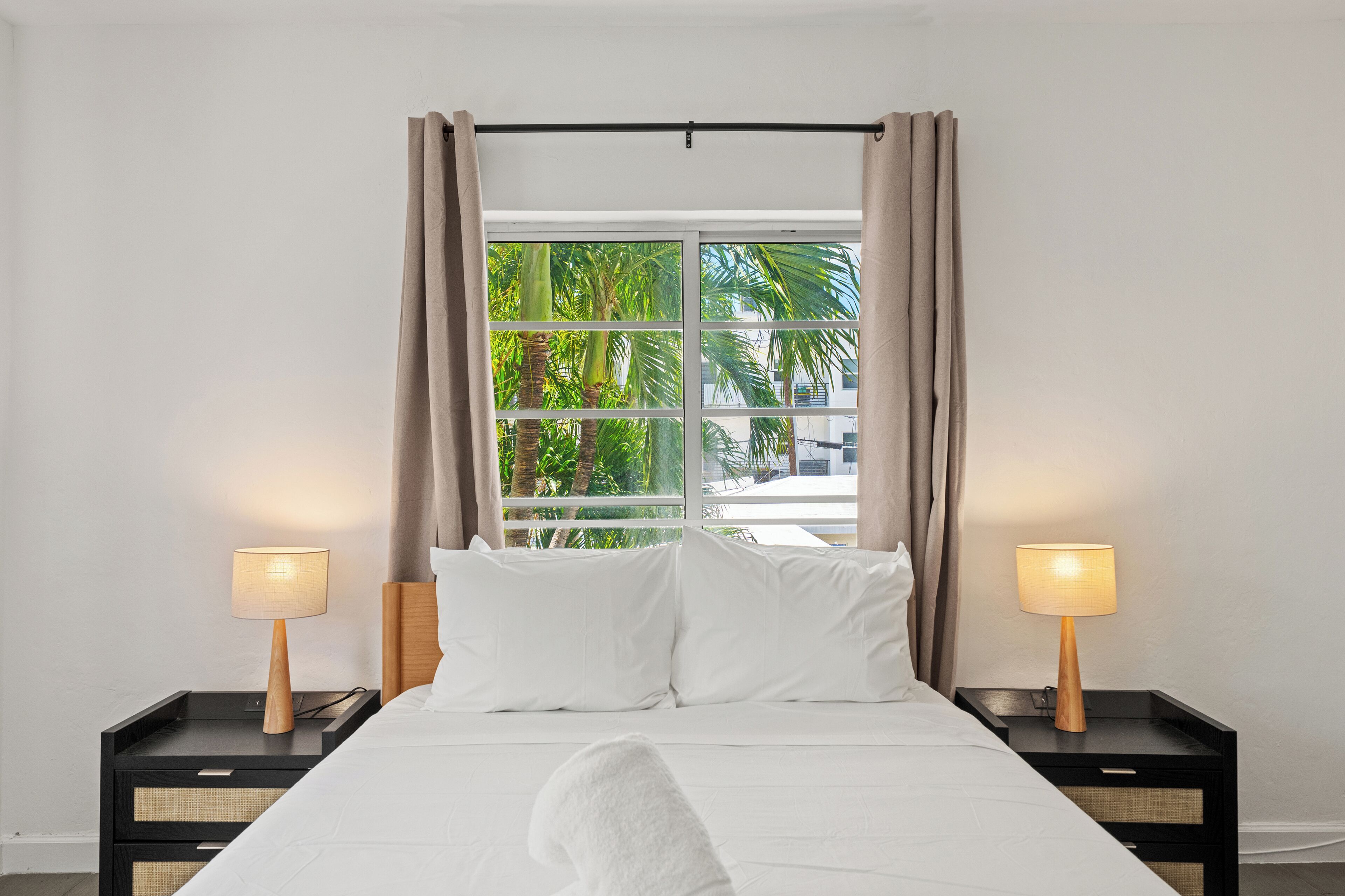 A hotel room with a bed, two bedside tables, lamps, and a window with curtains.