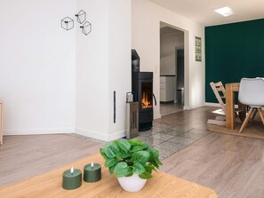 A modern living room with a fireplace, a dining area with a table and chairs, and a kitchen in the background. - 4 Person Holiday Home in Orum Djurs (Ørum Djurs)