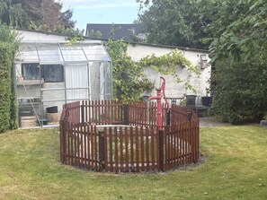A fenced garden area with a greenhouse, a red chair, and a white building with ivy. - 4 Person Holiday Home in Orum Djurs (Ørum Djurs)