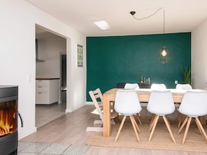 A modern dining area with a wooden table and white chairs, a green accent wall, and a fireplace.