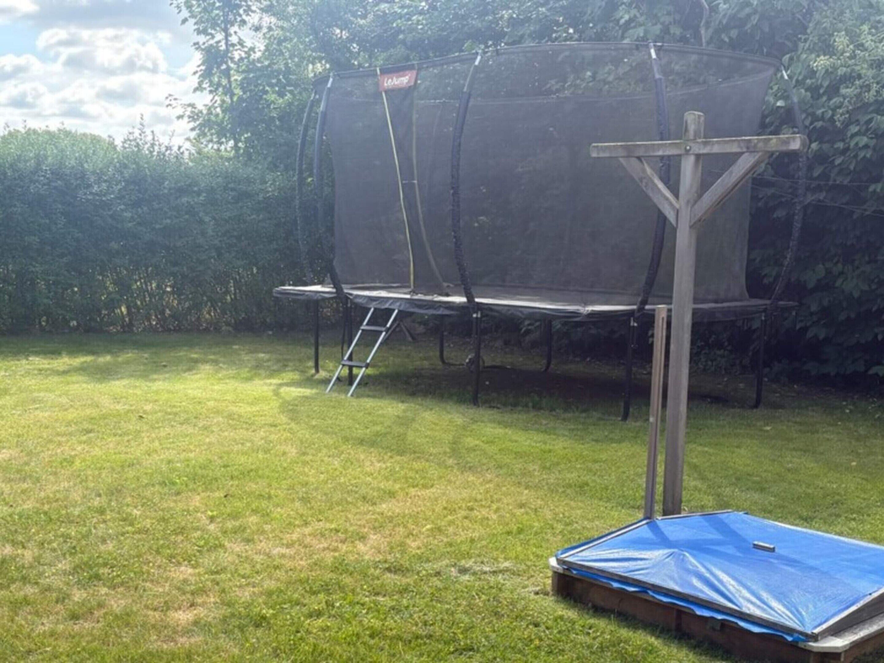 A trampoline with a safety net, a ladder, and a blue tarp on the ground.