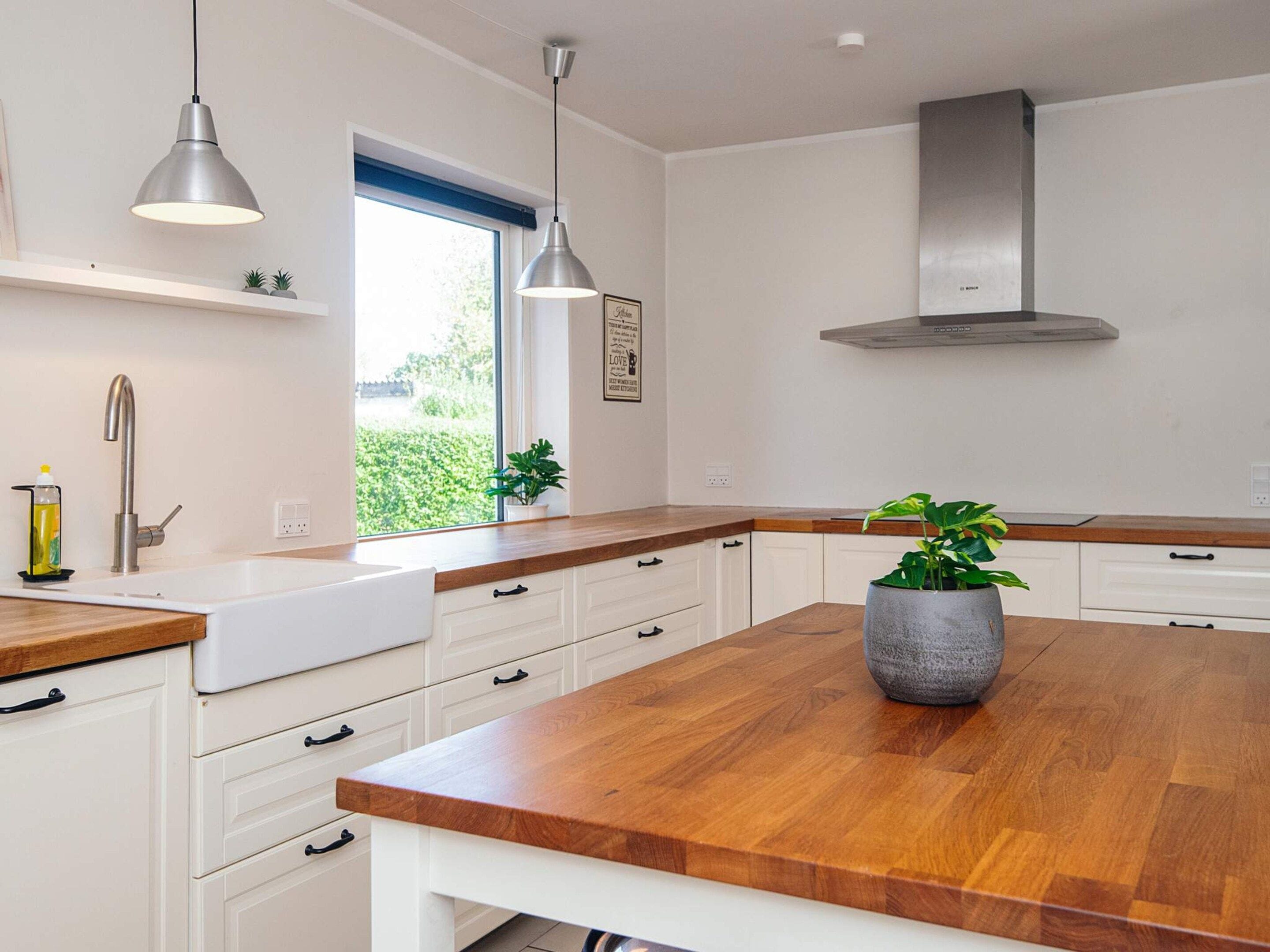 A modern kitchen with white cabinetry, a wooden countertop, pendant lighting, and a stainless steel range hood.