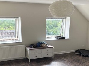 A room with two windows, a white radiator, a white dresser with drawers, and a hanging light fixture. - 4 Person Holiday Home in Orum Djurs (Ørum Djurs)