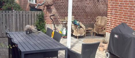 An outdoor patio with a table and chairs, a covered seating area, and a barbecue grill.