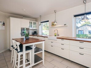 A modern kitchen with white cabinetry, a wooden countertop, and a dining area with chairs. - 4 Person Holiday Home in Orum Djurs (Ørum Djurs)