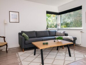 A modern living room with a grey sofa, a wooden coffee table, and a view of greenery through a window.