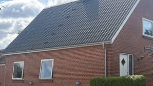 A red brick building with a sloped roof, a white door, and a bench outside. - 4 Person Holiday Home in Orum Djurs (Ørum Djurs)