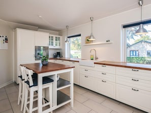 A modern kitchen with white cabinetry, a wooden countertop, and a dining area with white chairs.
