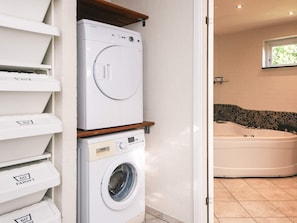 Une buanderie équipée d’une pile de machines à laver et de sèche-linge, d’une petite étagère et donnant sur une salle de bain avec une baignoire.