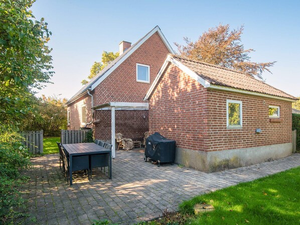 A brick house with a covered patio, a grill, and a table with chairs.