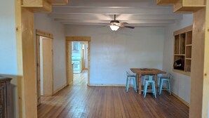 Une pièce spacieuse avec un plancher en bois, un ventilateur de plafond et un coin repas comprenant une table et des chaises.