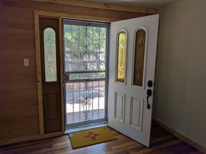 A wooden-framed door with a glass panel and decorative metalwork, leading to an outdoor area with a wooden deck and a yellow doormat. - Casa Tomas - Beautifully restored Adobe from the 1800's.  True NM. (Albuquerque)