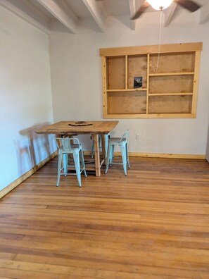 A room with a wooden table and two chairs, a wooden shelf unit, and a ceiling fan. - Casa Tomas - Beautifully restored Adobe from the 1800's.  True NM. (Albuquerque)