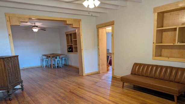 Une pièce avec un plancher en bois, un canapé en cuir marron, une table à manger avec des chaises et un ventilateur de plafond.