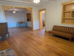 A room with a wooden floor, a brown leather sofa, a dining table with chairs, and a ceiling fan. - Casa Tomas - Beautifully restored Adobe from the 1800's.  True NM. (Albuquerque)