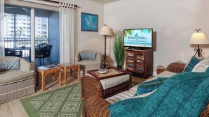 A hotel room with a balcony, a television, wicker furniture, and a green patterned rug. - Beautiful Beachfront 2 Bedroom 2 Full Baths (Bonita Springs)