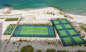 Ein Tennisplatzkomplex mit mehreren Plätzen, umgeben von einem Sandstrand und dem Ozean.