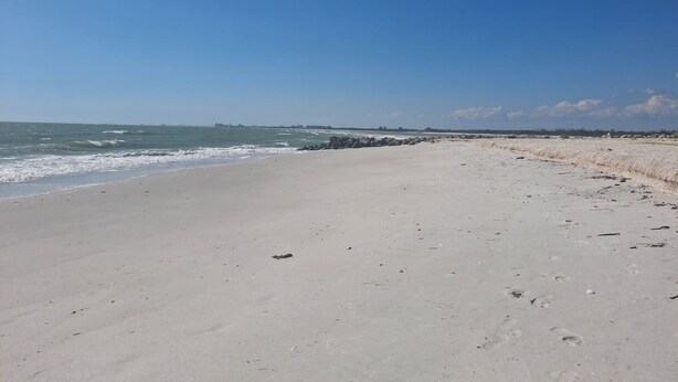 A wide sandy beach with gentle waves, a clear sky, and distant buildings. - Beautiful Beachfront 2 Bedroom 2 Full Baths (Bonita Springs)