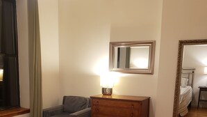 A hotel room with a bed, a dresser, a chair, a mirror, and a window with curtains.