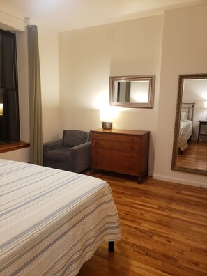 A hotel room with a bed, a dresser, a chair, a mirror, and a window with curtains.