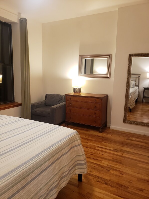 Una habitación de hotel con cama, cómoda, silla, espejo y ventana con cortinas.
