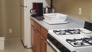 A kitchen with wooden cabinets, a white refrigerator, a stove, and a kettle on the countertop.