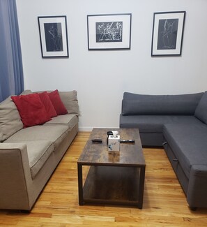 A living room with a sofa, a coffee table, and three framed artworks on the wall. - Peaceful 1-bedroom apartment with AC in vibrant New York (New York)