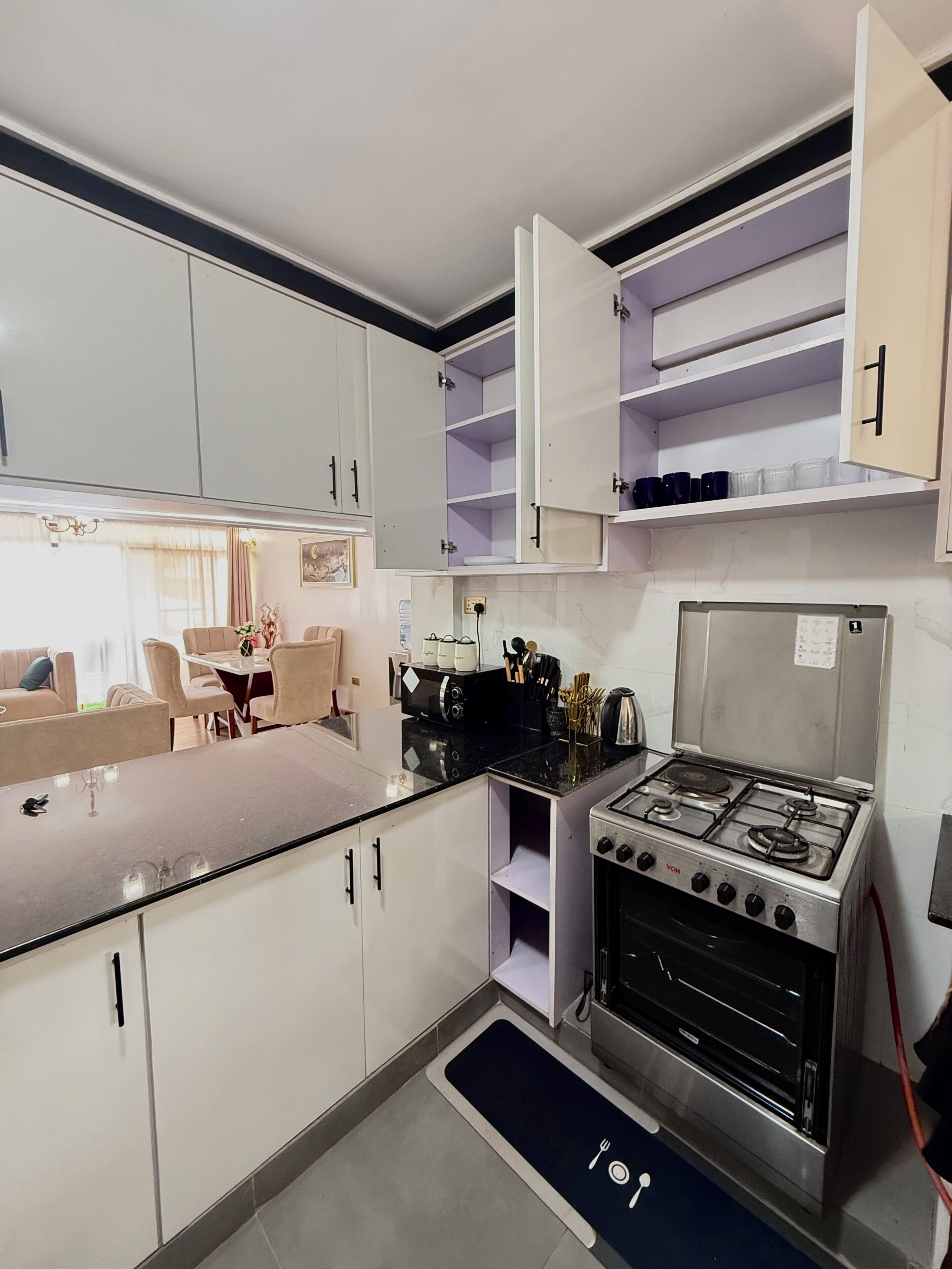 Une cuisine compacte avec des meubles blancs, une cuisinière à gaz et un coin repas comprenant une table et des chaises.