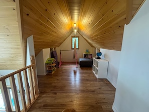Una habitación de madera en el ático, con techo inclinado, una ventana, una escalera de madera y una estantería.