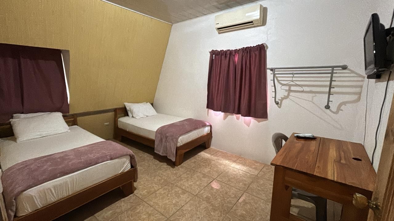 Un dormitorio con dos camas, una mesa de madera, un televisor y una ventana con cortinas.