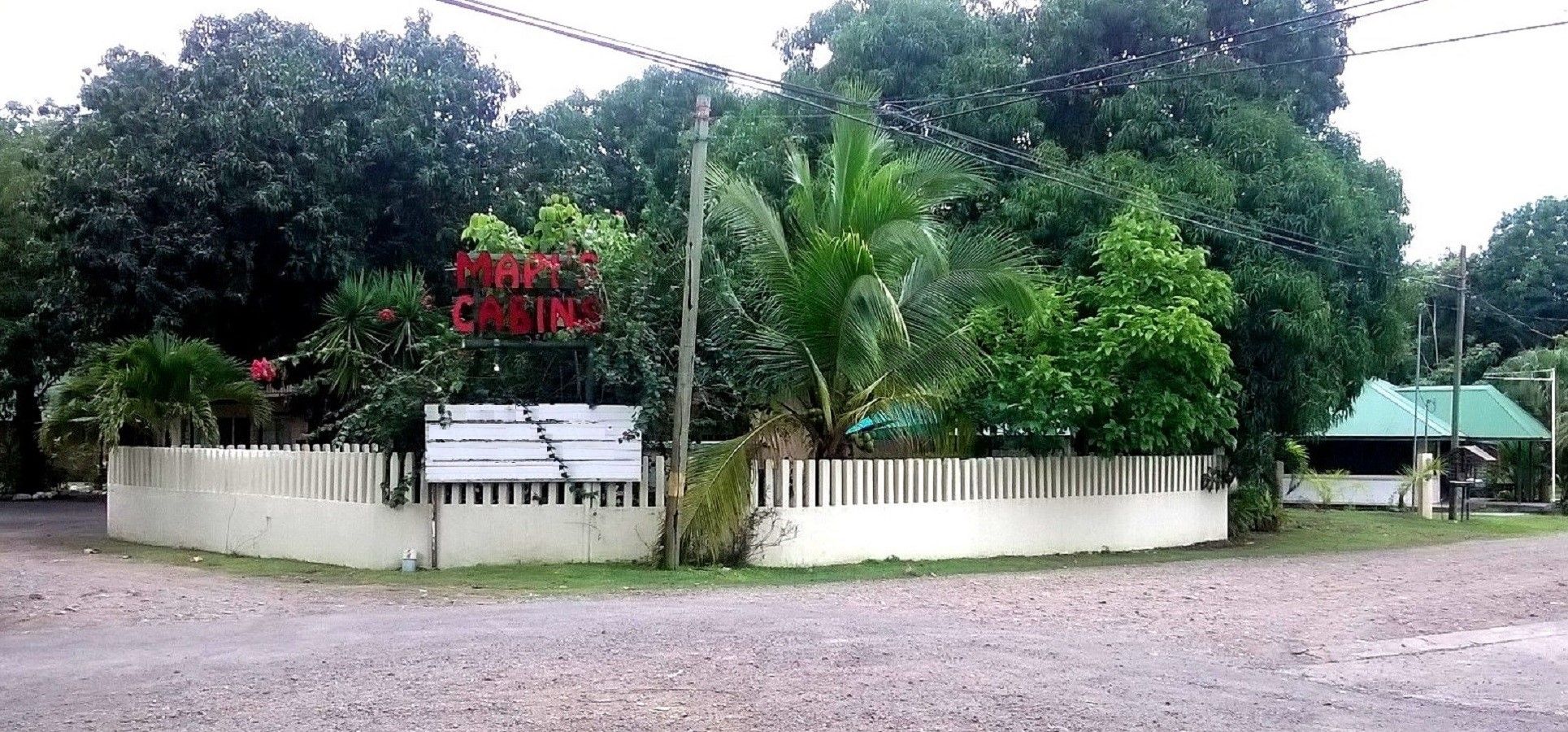 A sign for a hotel with a white fence and lush greenery in the background.