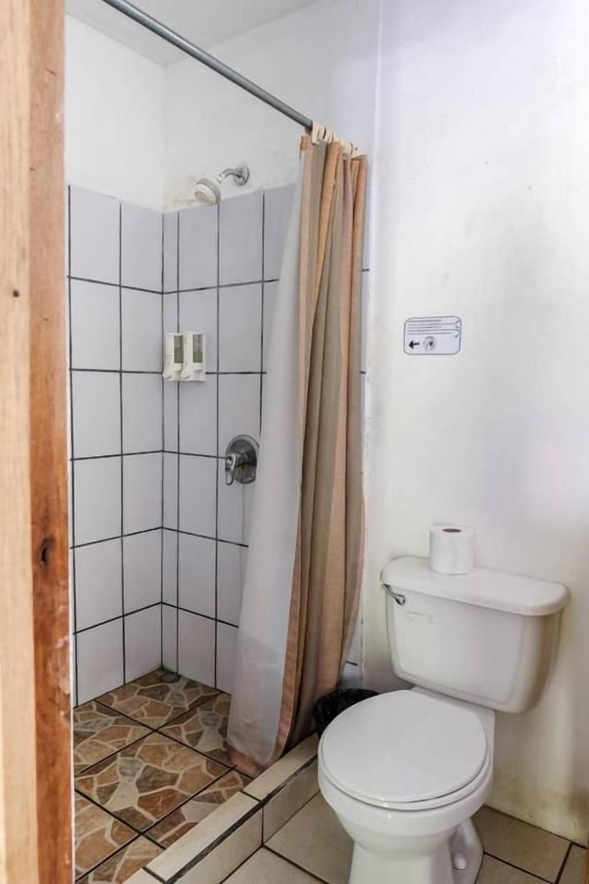 A bathroom with a shower, toilet, and tiled floor.