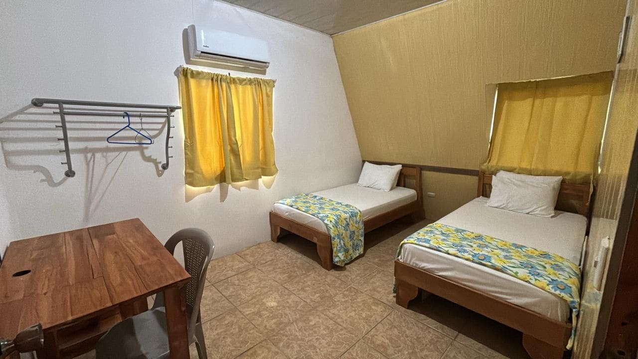Una habitación con dos camas, una mesita y una silla.