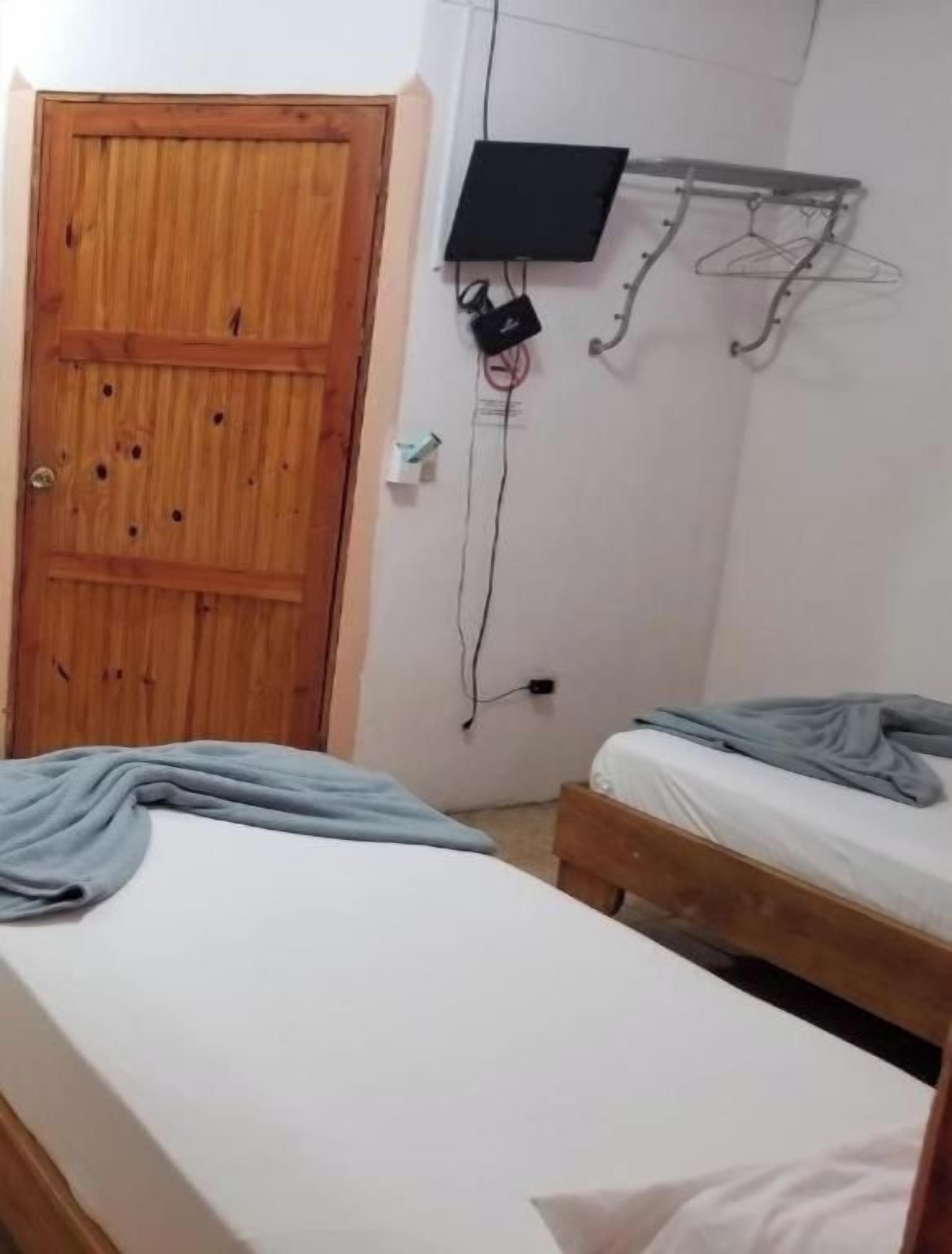 Un dormitorio con dos camas, una puerta de madera, un televisor montado en la pared y un tendedero.