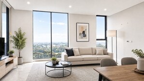 Ein modernes Wohnzimmer mit einer Couch, einem Couchtisch und einem Fernseher auf einem Holzschrank. Ein großes Fenster bietet Blick auf die Stadt.