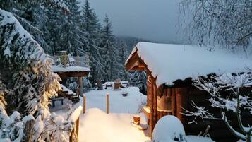 Eine verschneite Holzhütte mit Schnee bedecktem Dach und einer Holterrasse.