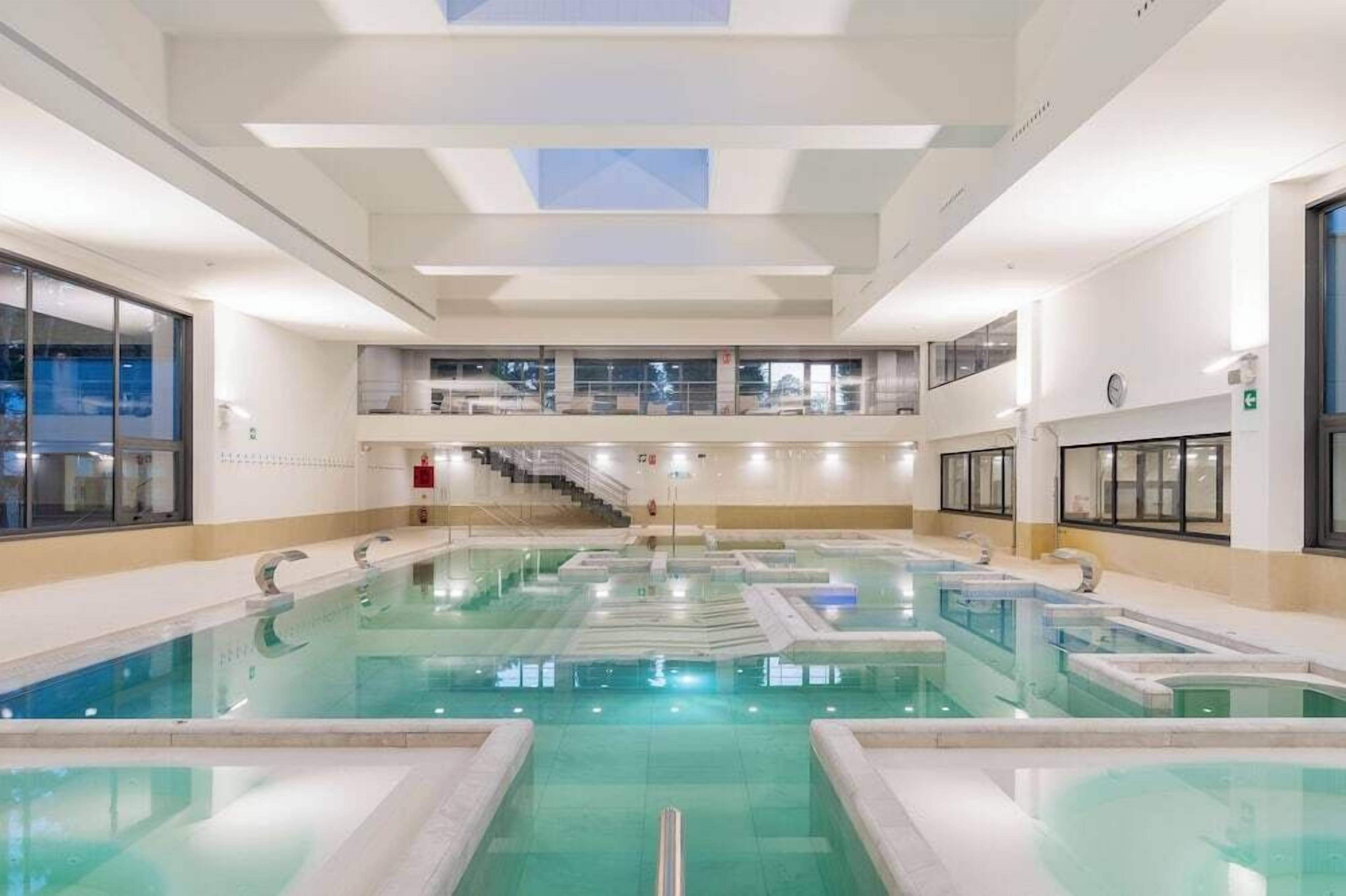 Una gran piscina interior amb diverses línies, una escala que mena a un nivell superior i un rellotge a la paret.