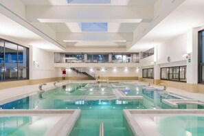 A large indoor swimming pool with multiple lanes, a staircase leading to an upper level, and a clock on the wall. - Balneario de Guitiriz (Guitiriz)