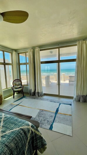 A room with a large window overlooking a beach, a bed, a chair, and a rug. - Silver Seas – Oceanfront Home in Santo Tomás, Mexico (Playa Santo Tomás)