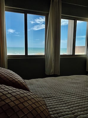 A bed with a view of the ocean through a window.