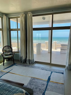 A room with large windows overlooking a beach, a chair with a cushion, and a patterned rug. - Silver Seas – Oceanfront Home in Santo Tomás, Mexico (Playa Santo Tomás)
