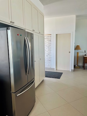 A modern kitchen with a stainless steel refrigerator, white cabinets, and a tiled floor.