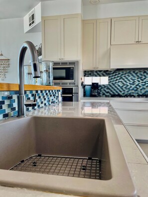 A modern kitchen with a stainless steel sink, a Bosch microwave, and a tiled backsplash.