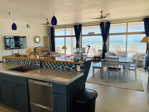 Une cuisine moderne dotée d’un îlot central, d’un coin repas offrant une vue sur la plage et d’un ventilateur de plafond.