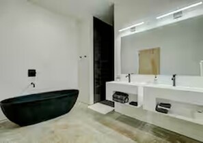 Ein modernes Badezimmer mit freistehender Badewanne, einem großen Spiegel und einem weißen Waschtisch.